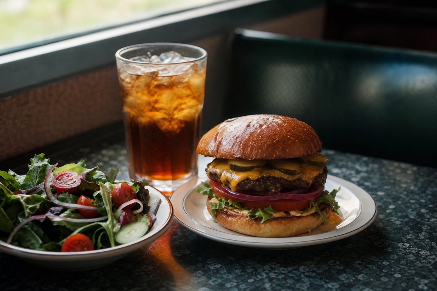 A diner-style table with a burger, a side salad and a glass of iced tea